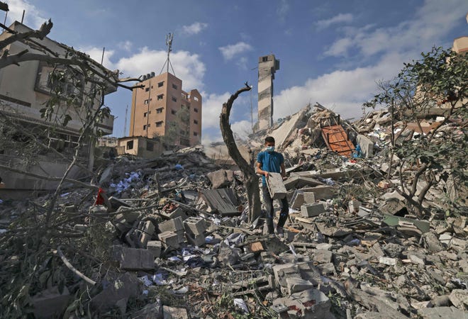 A Palestinian youth looks for salvageable items amid the rubble of the Kuhail building which was destroyed in an early morning Israeli airstrike on Gaza City on May 18, 2021. The building had a printshop and university accessories and books storage facility for educational institutes in Gaza as well as a mosque.